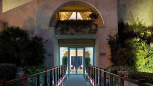 A corridor leading to a building entrance with a glass door, surrounded by a wooden railing and illuminated by ground lights. - L'Ea Bianca Luxury Resort (Arzachena)