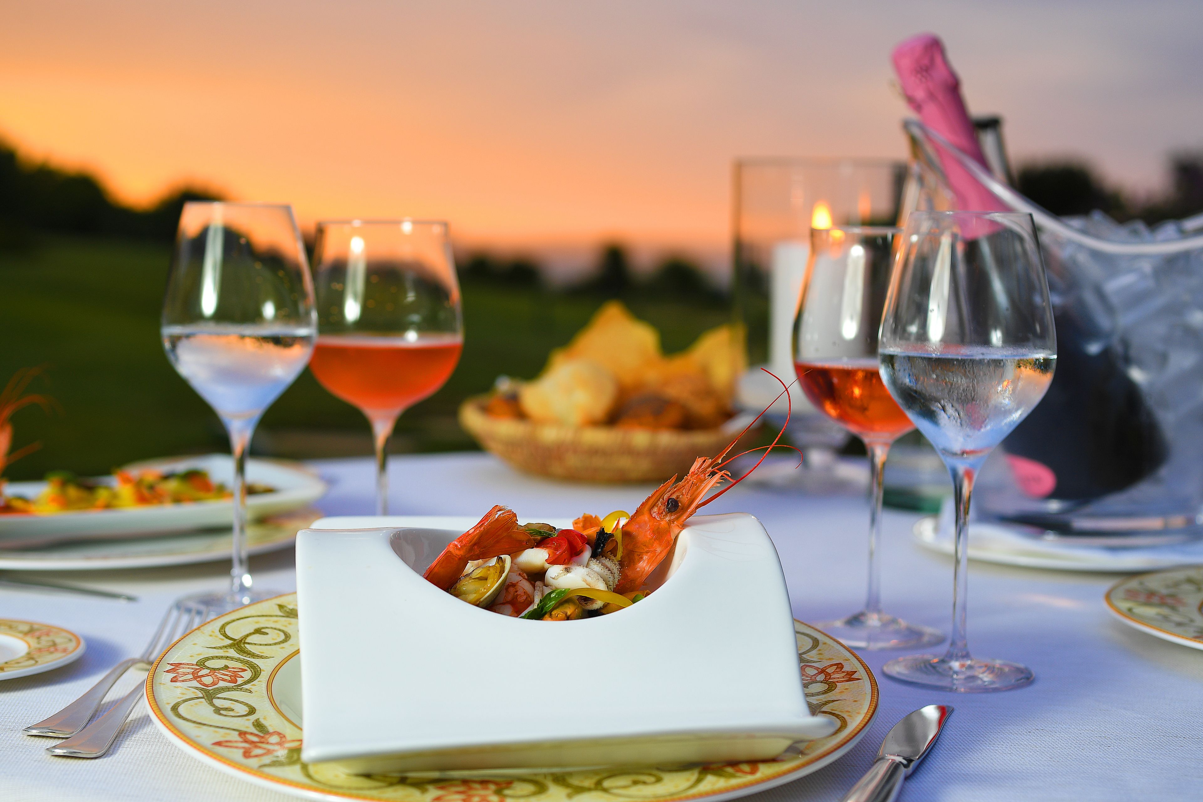 Mesa posta para o jantar com copos de vinho, um prato de camarão e uma vela.