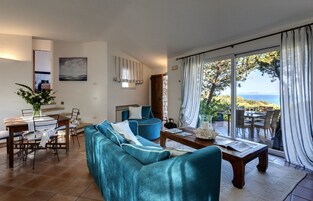 Amplia sala de estar con sofá, mesa de comedor y sillas, una mesa de centro, y vista al mar a través de grandes ventanales.