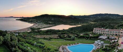 A resort with a swimming pool, lush greenery, and a view of the sea.