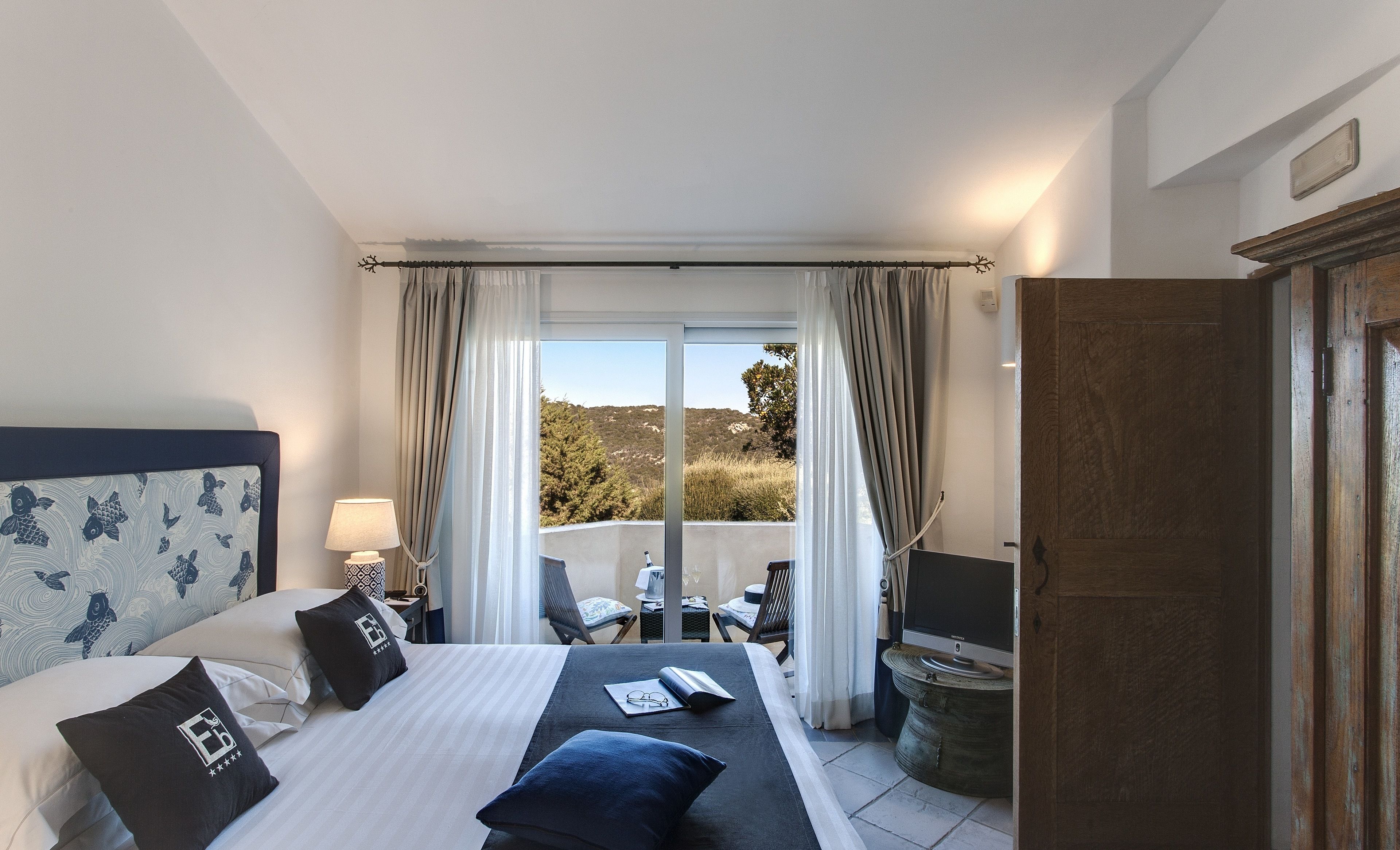 A hotel room with a bed, a desk, a chair, and a view of the outdoors.