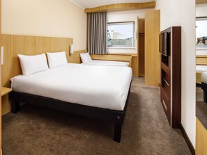 A hotel room with a large bed, a desk, a television, and a window with a city view.