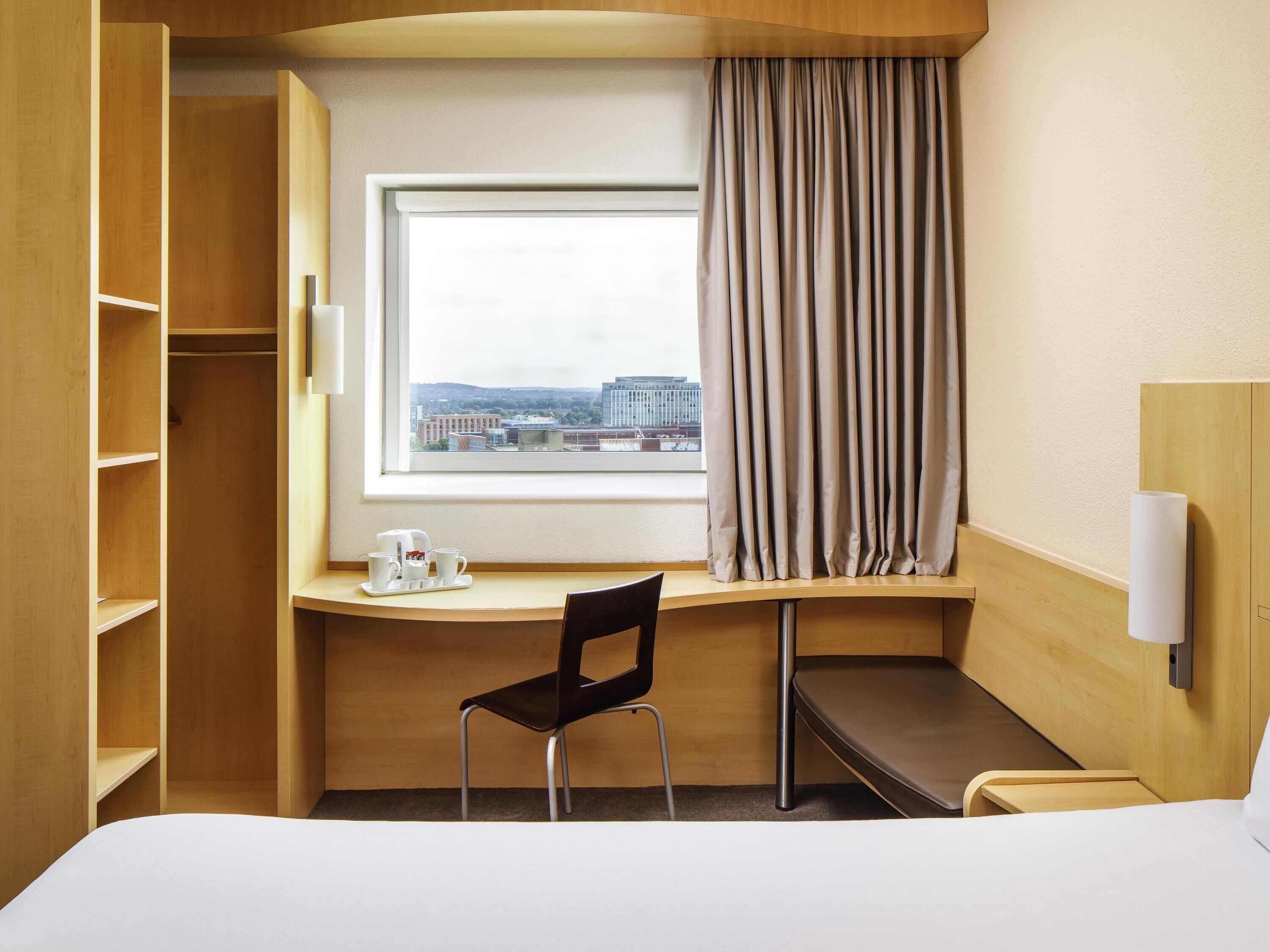 Quarto de hotel com escrivaninha, cadeira e cama.