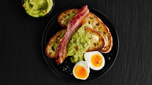 A plate with toasted bread, two halves of a boiled egg, and a piece of bacon, accompanied by a bowl of green spread. - ibis Nottingham Centre (Nottingham)