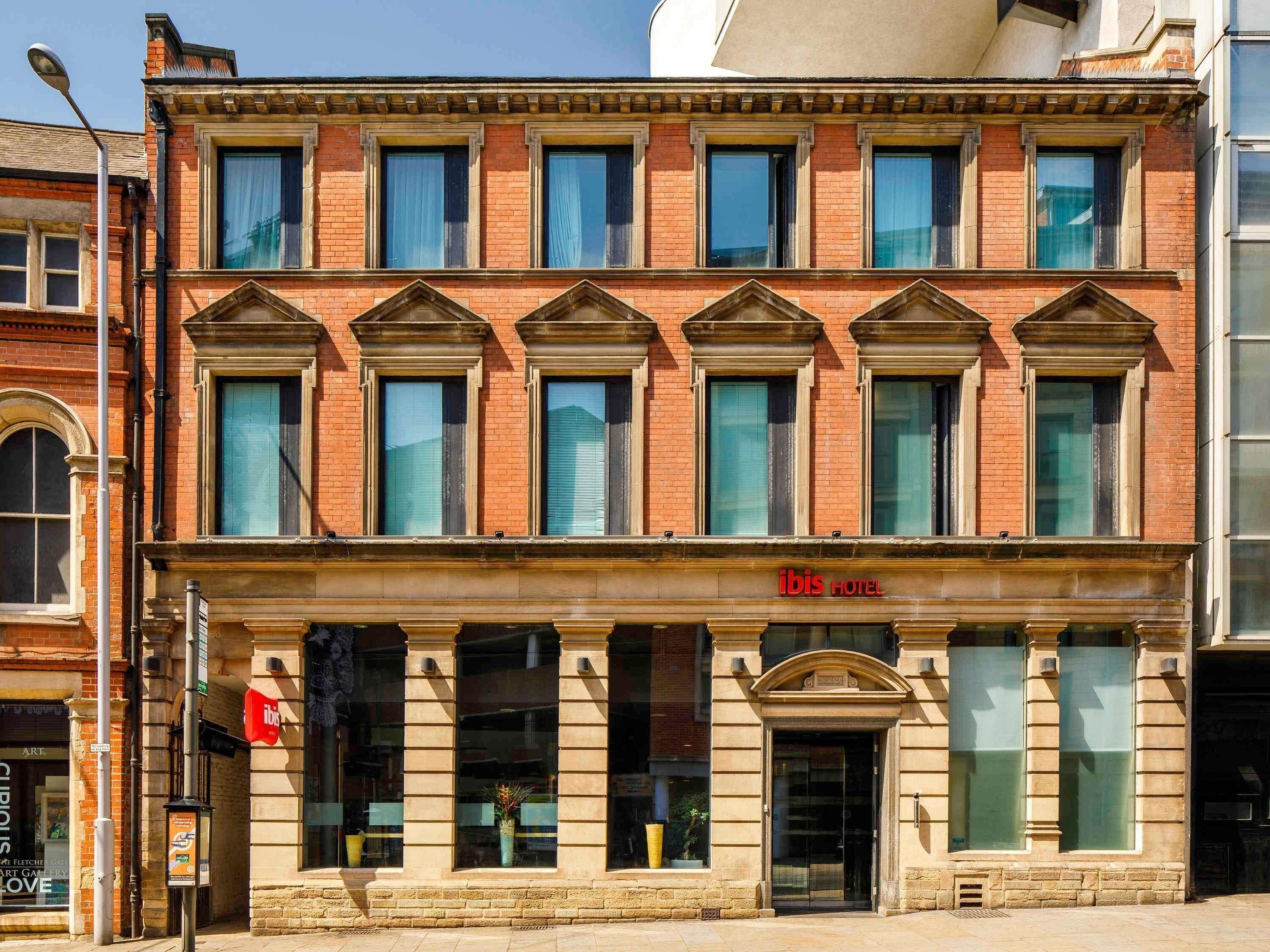 A two-story hotel with a classic facade, multiple windows, and a prominent 'ibis HOTEL' sign.