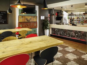 A restaurant interior with wooden tables, black and red chairs, hanging pendant lights, a bar area with bottles, and a menu board. - ibis Nottingham Centre (Nottingham)