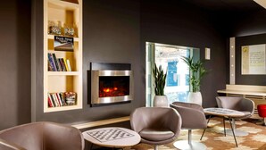 A modern lounge area with leather chairs, a fireplace, bookshelves, and a view through a large window. - ibis Nottingham Centre (Nottingham)