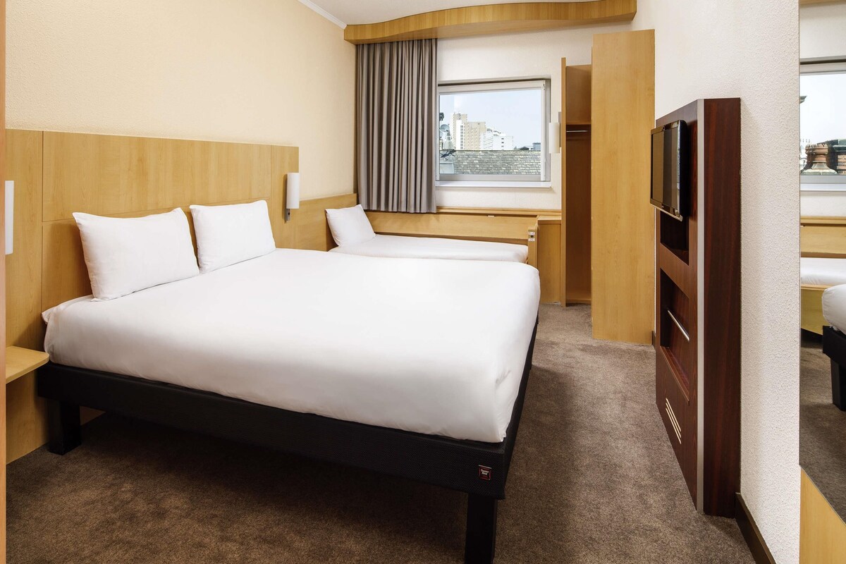 Habitación de hotel con una cama grande, un escritorio, un televisor y una ventana con vistas a la ciudad.