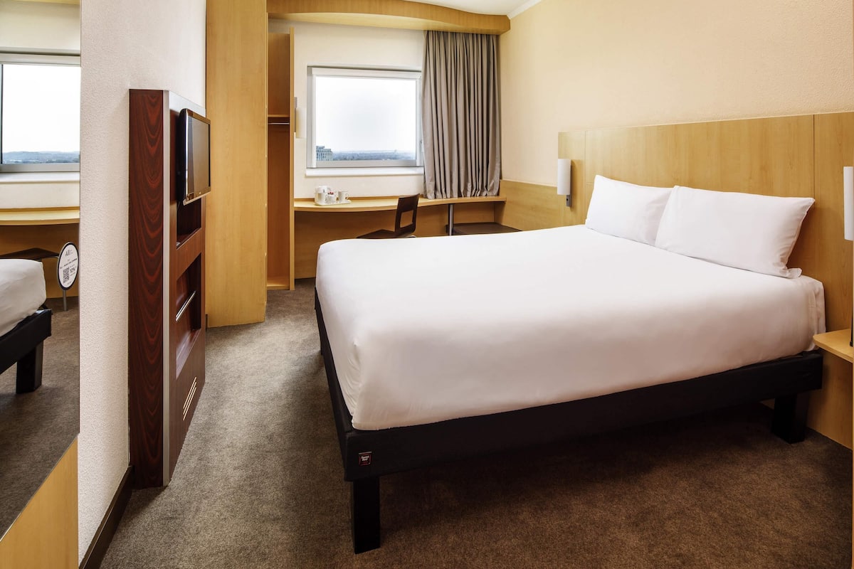 A hotel room with a bed, a desk, a TV, and a view of the city.