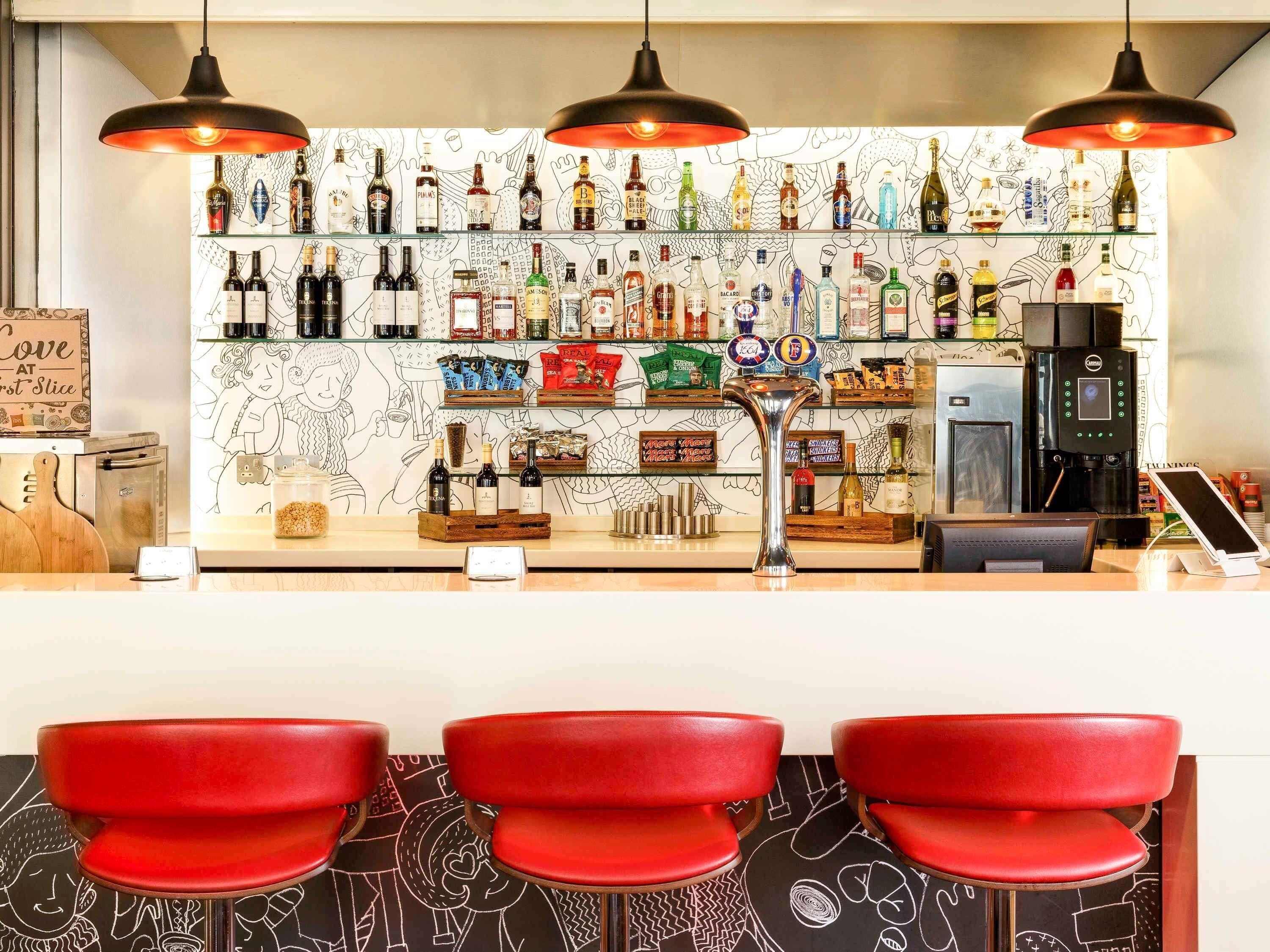 A bar area with a variety of liquor bottles, a coffee machine, and red bar stools.