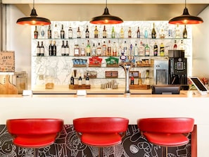 A bar area with a variety of liquor bottles, a coffee machine, and red bar stools.