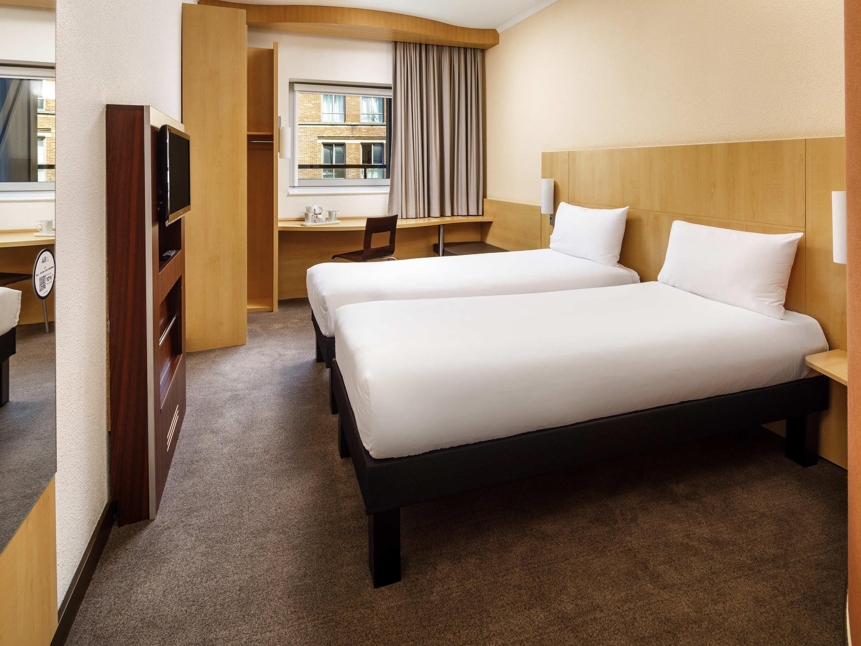 A hotel room with two beds, a desk, a chair, and a television.