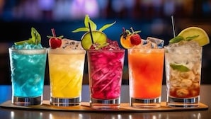 Fünf farbenfrohe Cocktails mit Garnituren auf einer Serviertablett.