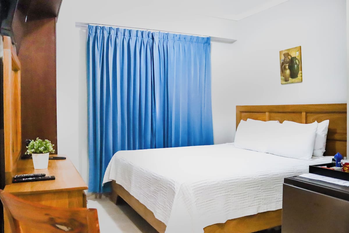 Ein Hotelzimmer mit Bett, Schreibtisch, Sessel, Blumentopf und einem Bild an der Wand.