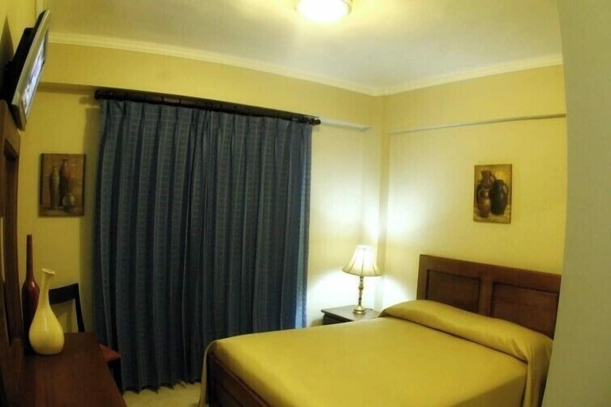 Ein Hotelzimmer mit einem Bett, einem Nachttisch mit Lampe, einem Vorhang und zwei an der Wand hängenden Bildern.