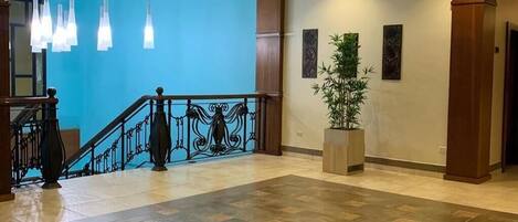 A spacious lobby with a tiled floor, a staircase with a railing, and hanging pendant lights.