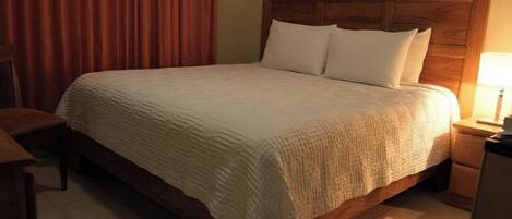 A neatly made bed with a wooden headboard, a bedside table with a lamp, and a chair.