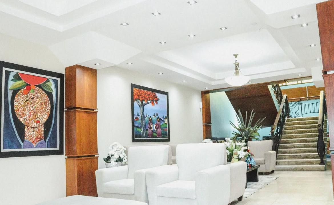 Een hotel lobby met witte leren banken, een trap en twee ingelijste kunstwerken aan de muren.
