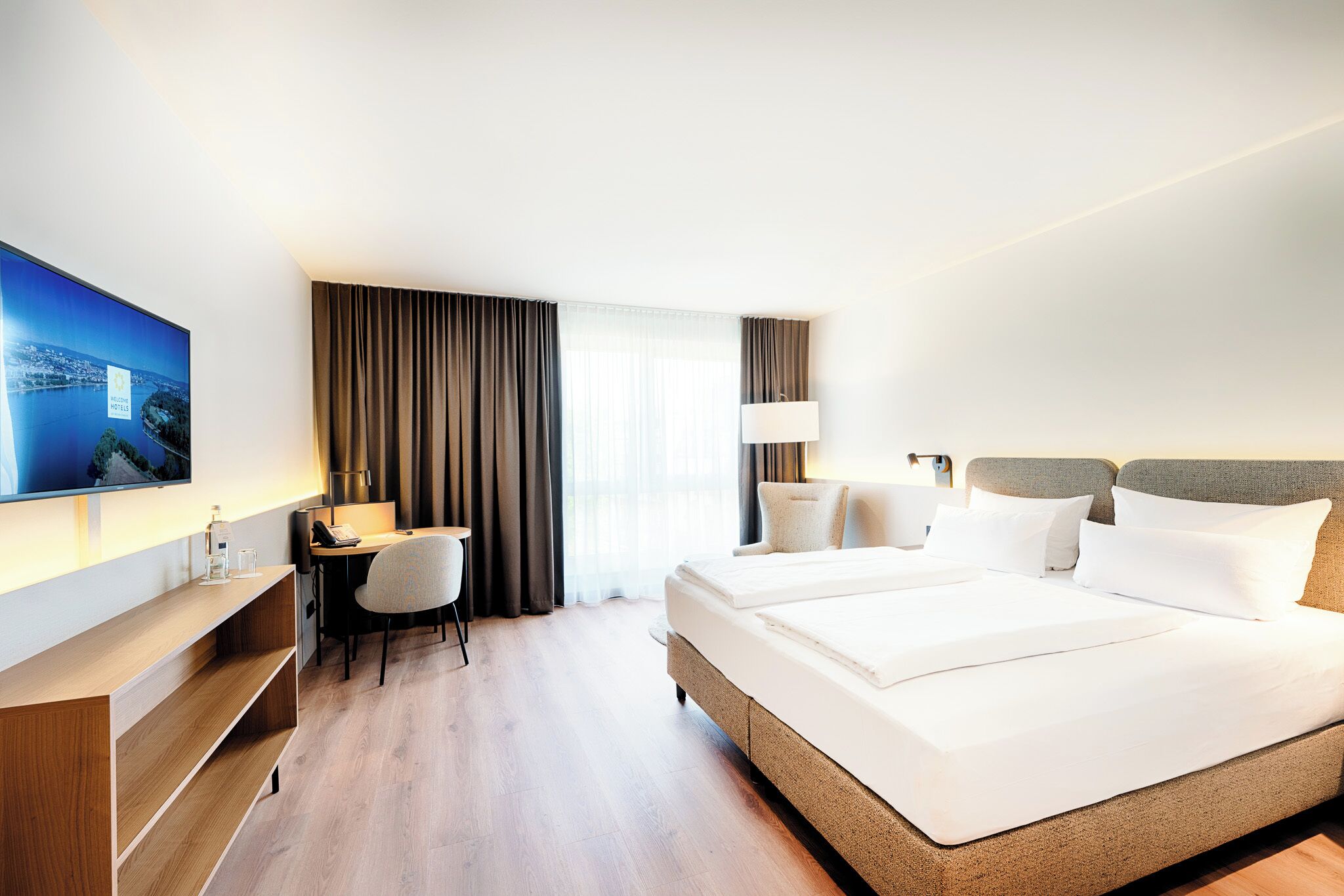 Une chambre d’hôtel équipée d’un lit, d’un bureau, d’une chaise, d’une télévision et d’une fenêtre avec des rideaux.