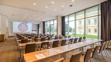 Un salón de conferencias con largas mesas, sillas y una pantalla de proyector que muestra "Welcome Hotel Darmstadt".