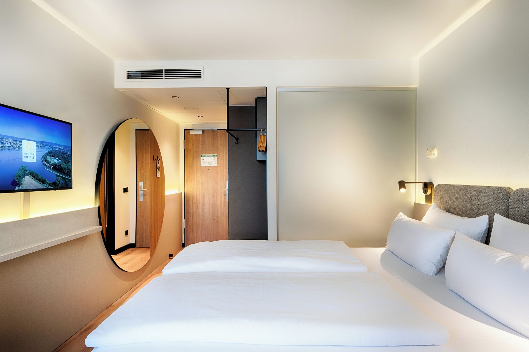 A modern hotel room with a large bed, a TV on the wall, and a view of the outdoors.