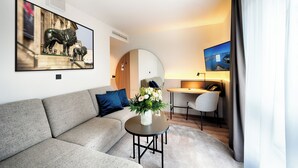 Un salón moderno con un sofá, una mesa de centro redonda con flores, un escritorio con una silla y un cuadro grande de toros en la pared.