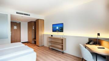 Habitación de hotel con cama, escritorio y silla, televisor montado en la pared y armario.