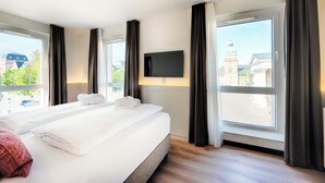 Habitación de hotel con una cama grande, un televisor de pantalla plana en la pared y vistas a la ciudad a través de las ventanas.