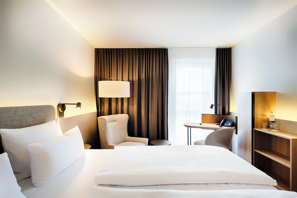 A hotel room with a large bed, a desk, a chair, a lamp, and a mirror.