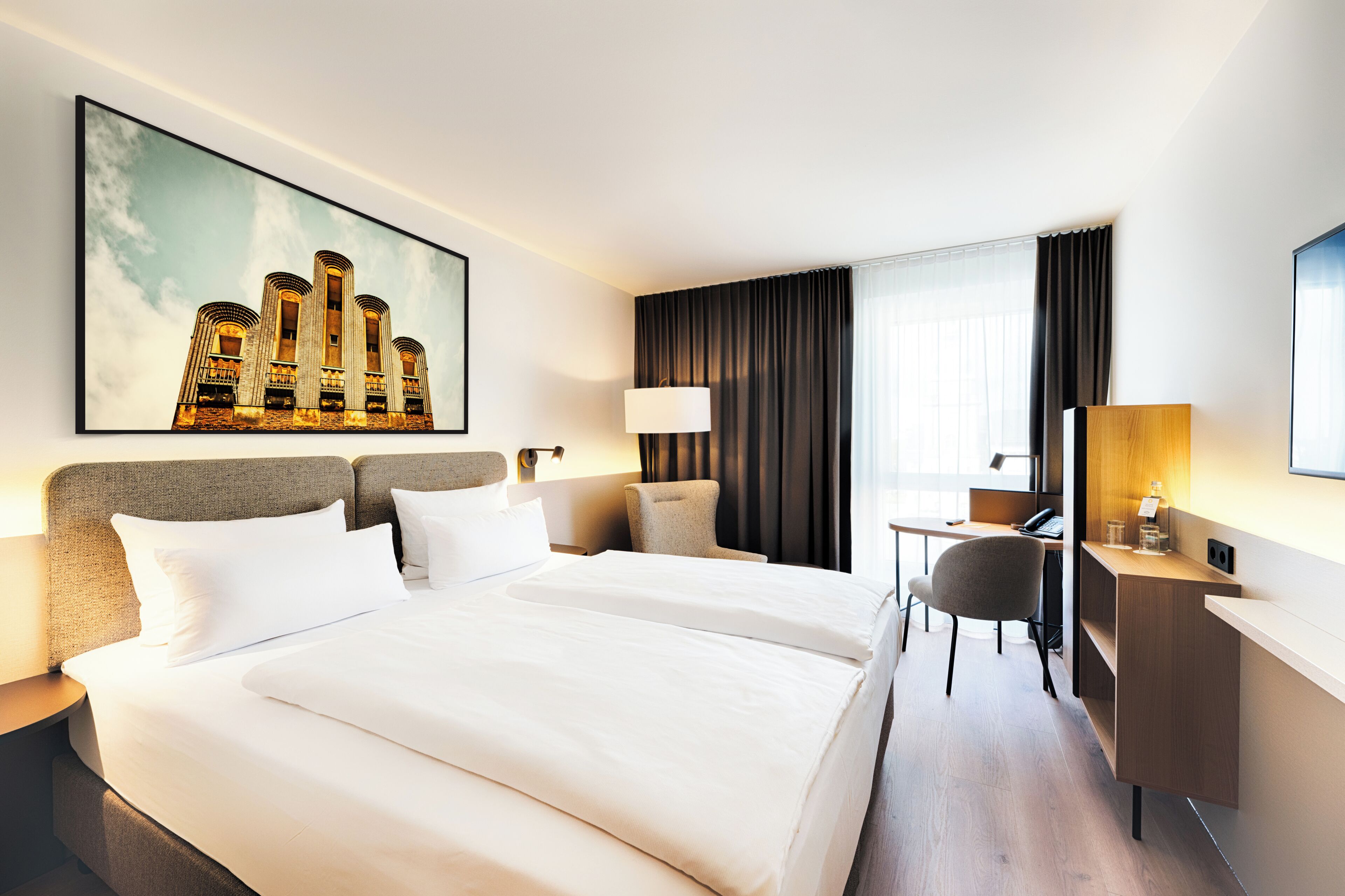 Habitación de hotel con una cama grande, un escritorio, una silla, una lámpara y un cuadro en la pared.