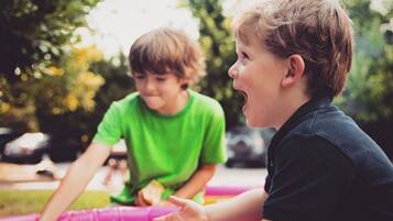 Two children playing with toys on a colorful mat outdoors.