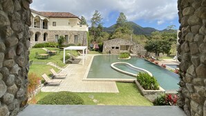 A stone archway framing a view of a courtyard with a swimming pool, outdoor seating, and a building with a tiled roof. - Los Mandarinos Hotel Boutique & Spa (El Valle de Anton)