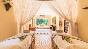 A spa room with two massage tables, a large window with a view of greenery, a ceiling fan, and a herringbone floor pattern. - Los Mandarinos Hotel Boutique & Spa (El Valle de Anton)