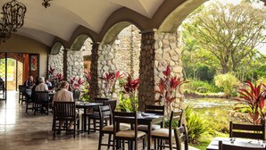 A restaurant with stone pillars, tables, and chairs, overlooking a pond and greenery. - Los Mandarinos Hotel Boutique & Spa (El Valle de Anton)
