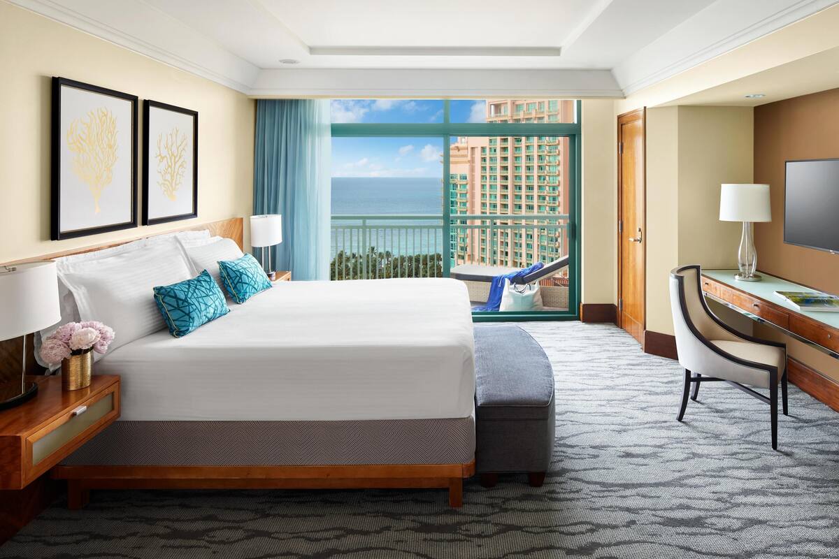 Una camera d'albergo con un letto grande, una scrivania, una sedia, una TV e vista sull'oceano.
