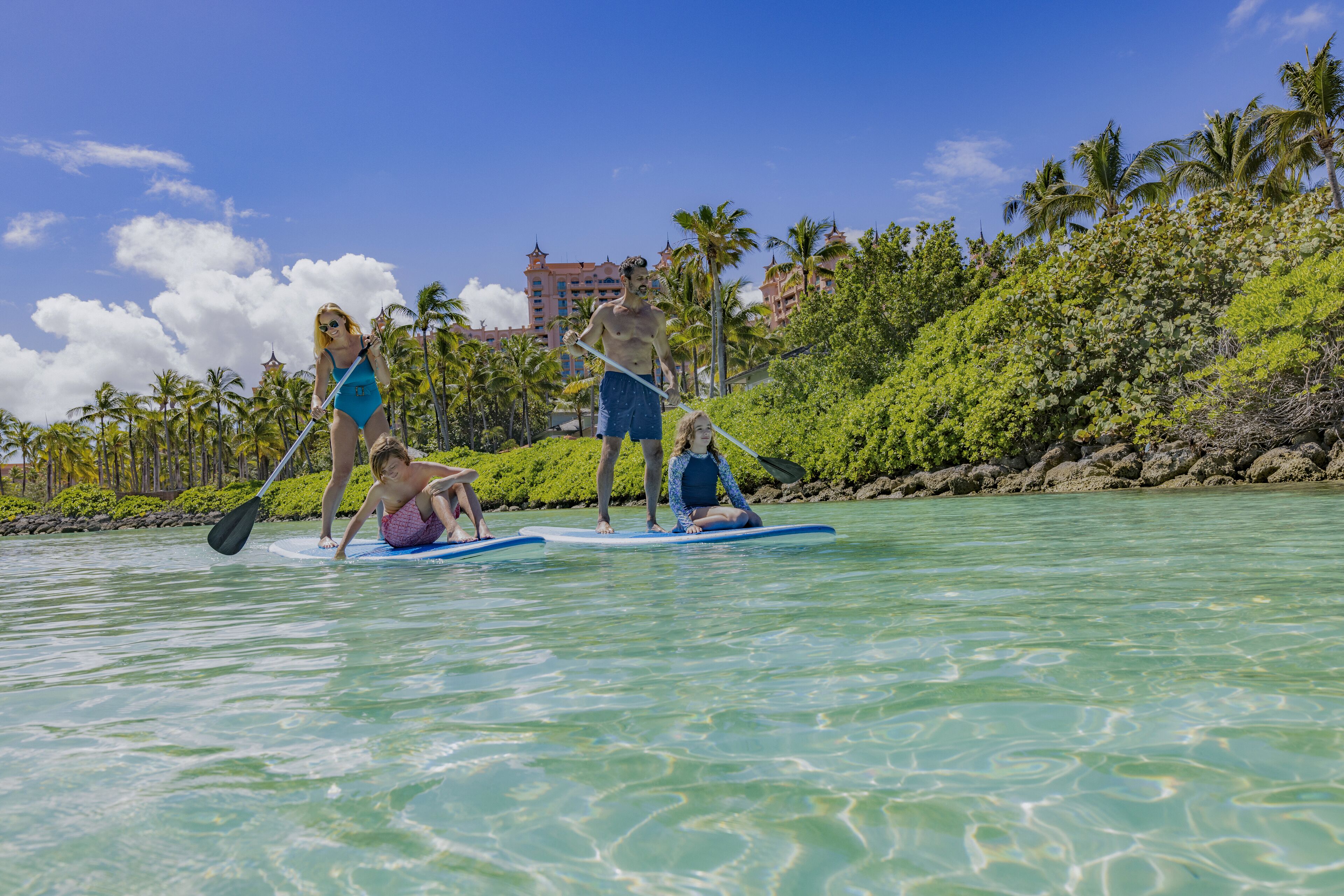 A group of people on paddleboards in clear water with a tropical backdrop and a large building in the distance.