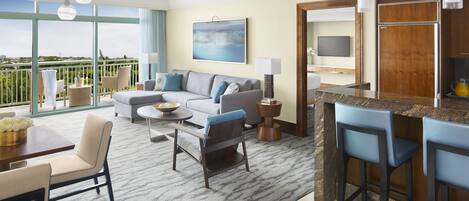 A modern hotel room with a balcony, a sofa, a dining area, and a kitchen counter.