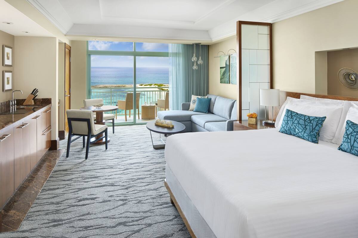 Una camera d'albergo con un ampio letto, una poltrona, un tavolo da pranzo e vista sull'oceano.