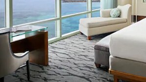 A hotel room with a large window offering a view of the ocean, a bed, a desk, and a chair. - The Reef at Atlantis (Paradise Island)
