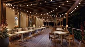 An outdoor dining area with wooden tables and chairs, string lights, and a view of the night sky. - The Reef at Atlantis (Paradise Island)