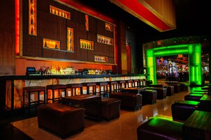 Una zona de bar con una barra alargada, varios taburetes y un área de estar con bancos acolchados.