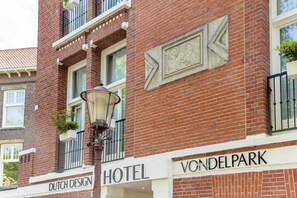 A brick building with 'DUTCH DESIGN HOTEL' and 'VONDEL PARK' signs, a street lamp, and a window with a plant. - Dutch Design Hotel Vondelpark (Amsterdam)