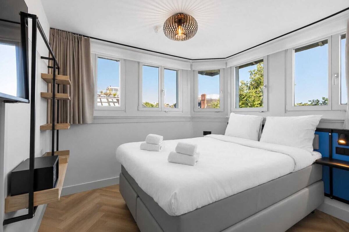 A modern bedroom with a large bed, a staircase, and multiple windows.