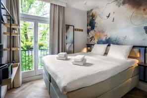 A modern bedroom with a large bed, a TV, a balcony with curtains, and a floral mural on the wall. - Dutch Design Hotel Vondelpark (Amsterdam)