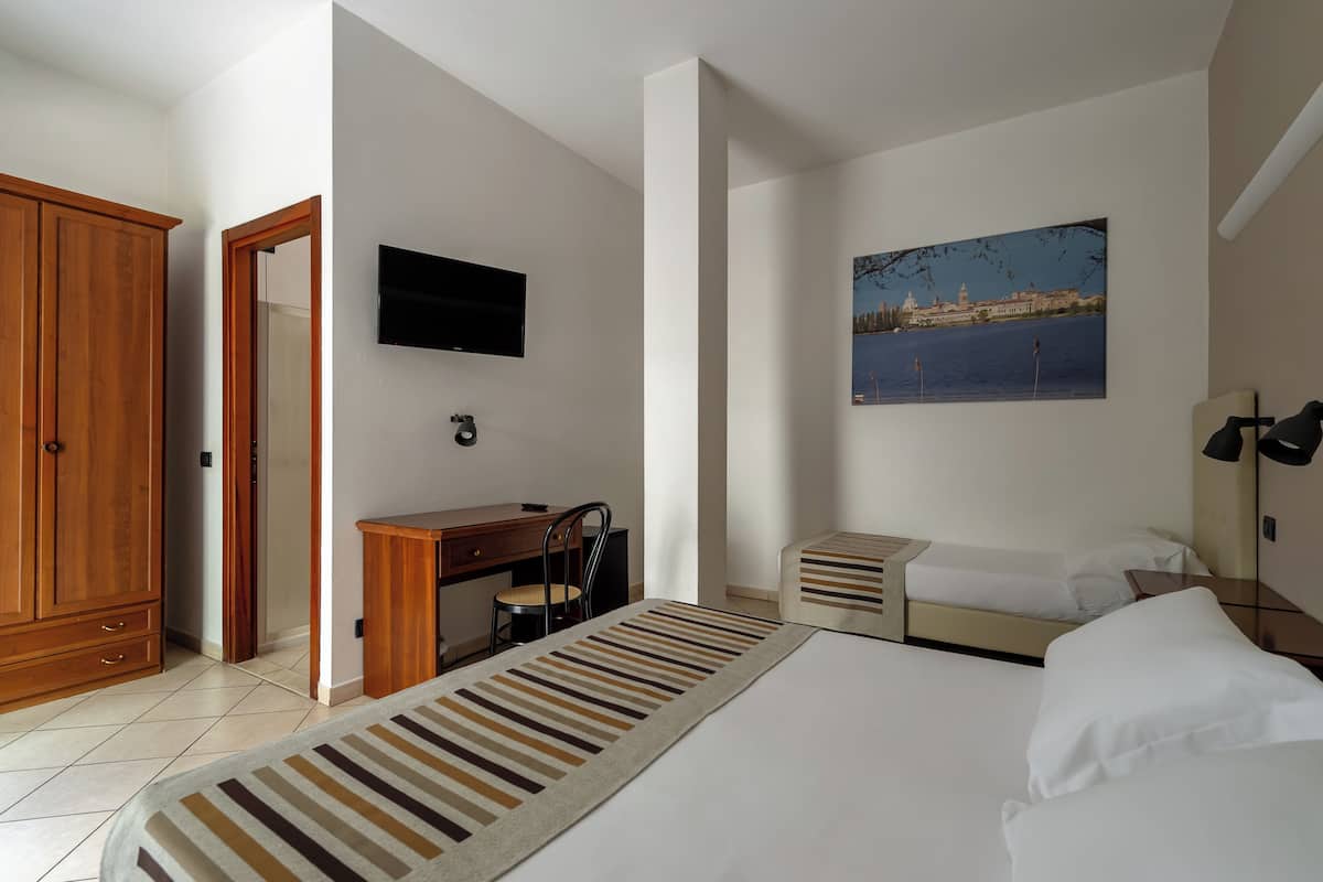 A hotel room with a bed, a desk, a chair, a television, and a painting of a cityscape.