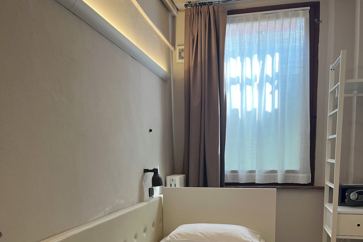 A neatly arranged bedroom with a bed, a bedside table, a lamp, and a window with curtains.
