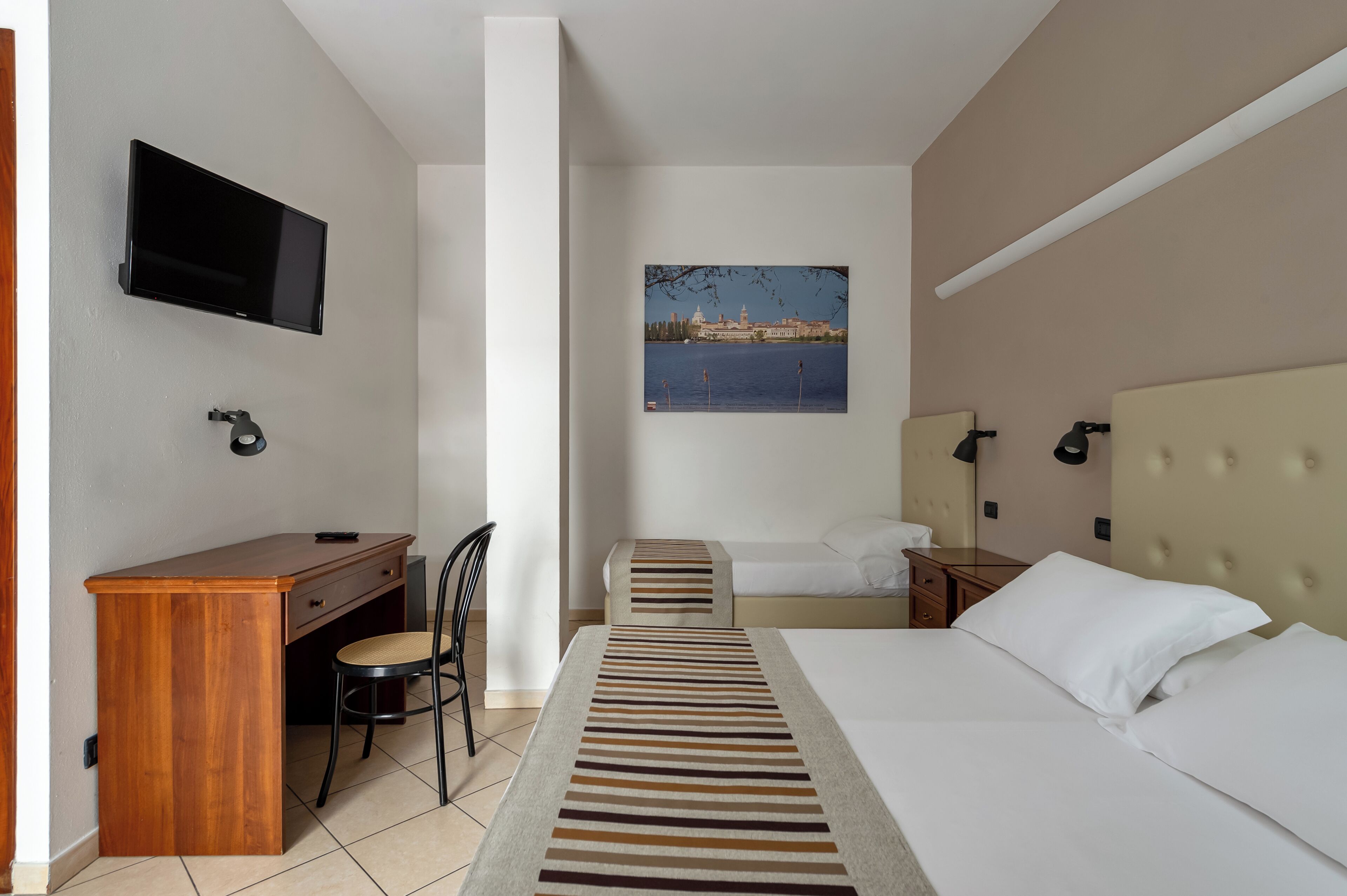 Una habitación de hotel con una cama, un escritorio, una silla, un televisor y un cuadro de un paisaje urbano.