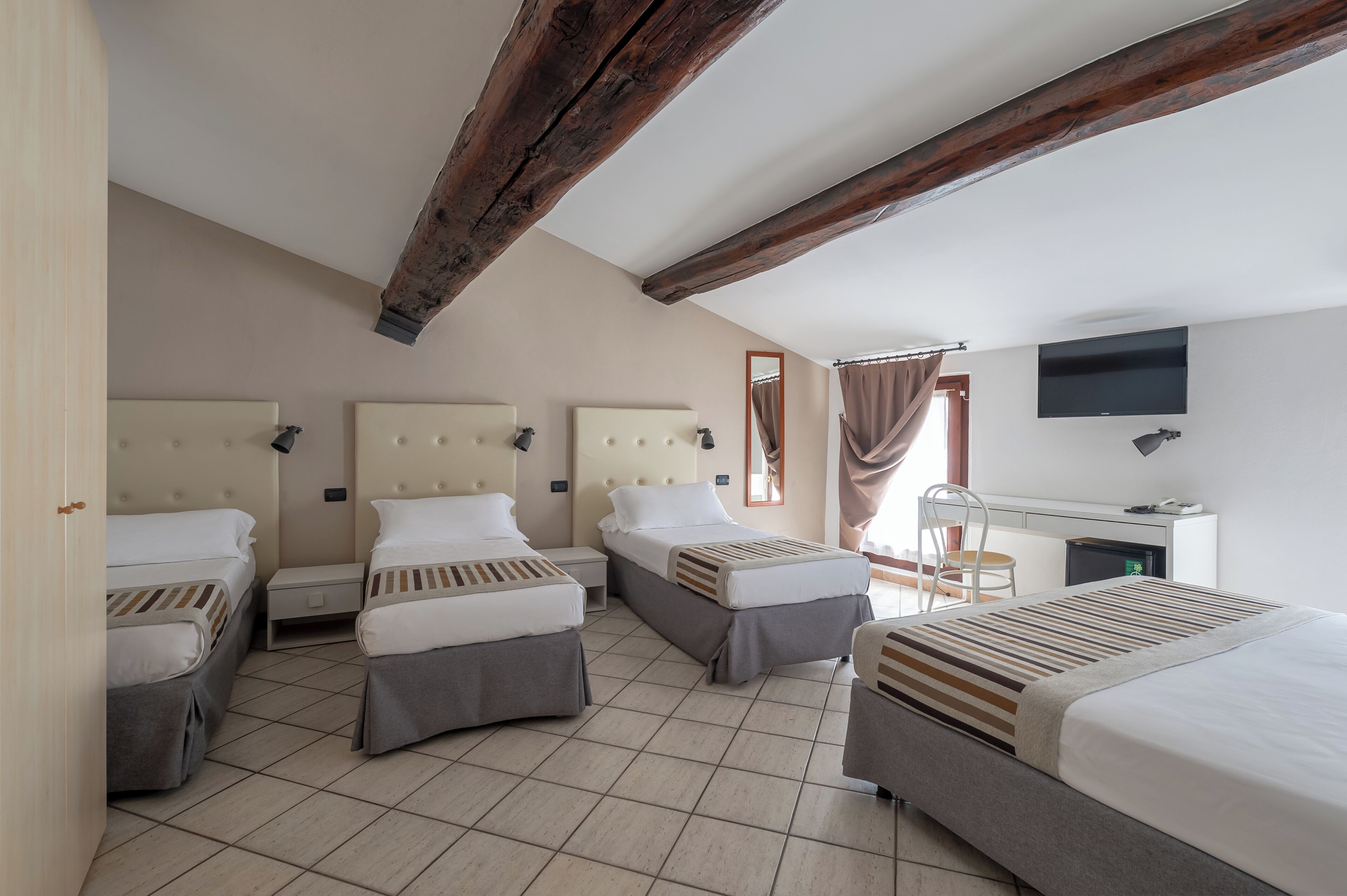 A hotel room with three beds, a desk, a chair, and a TV mounted on the wall.