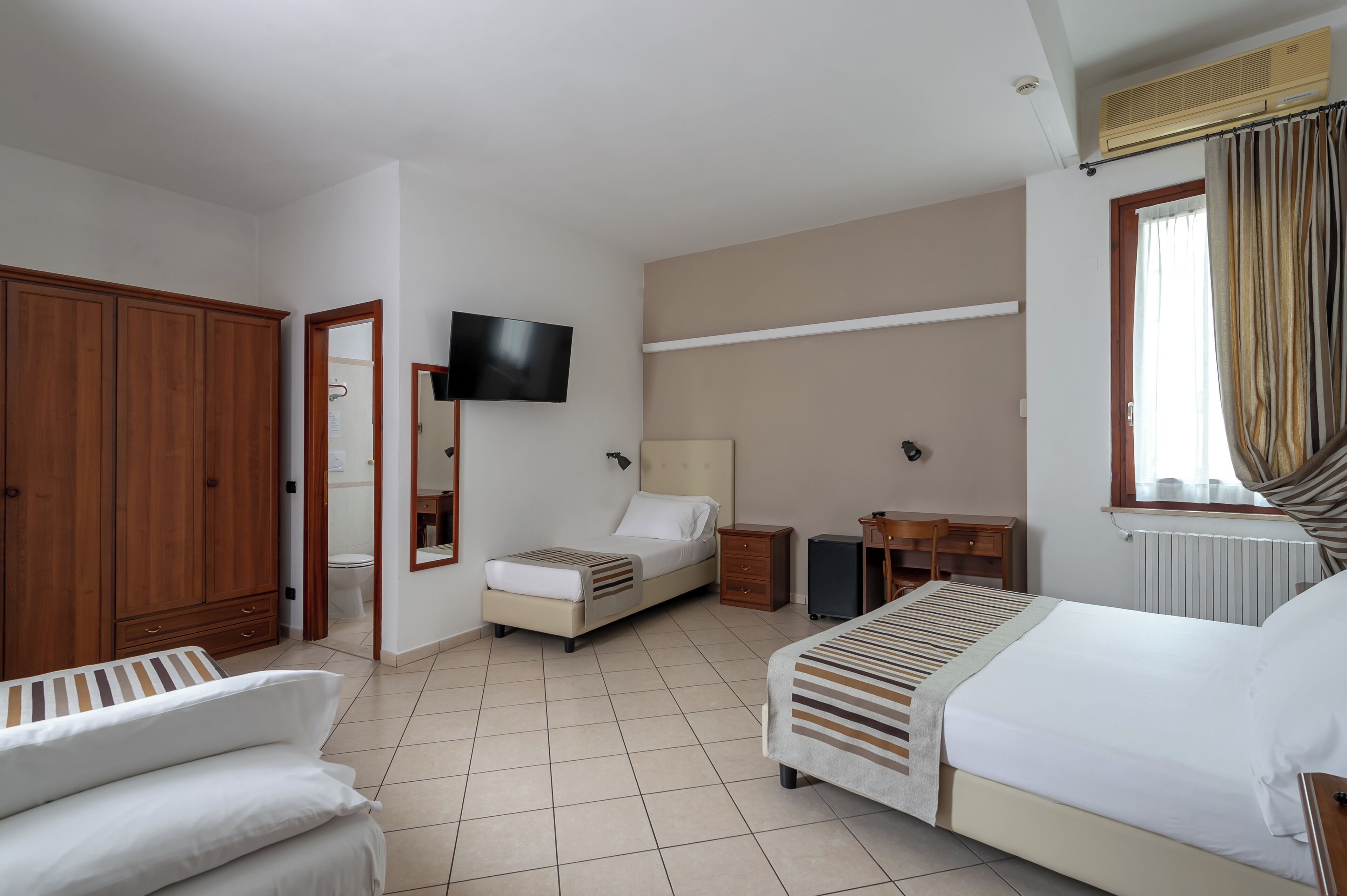 Una habitación de hotel con una cama, un escritorio, un televisor y un armario.
