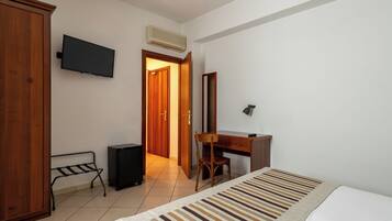 A hotel room with a bed, a desk, a chair, a wardrobe, a television, and an air conditioning unit.